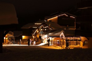 A photo of a house with christmas lights hanging from the roof at night. Family are outside